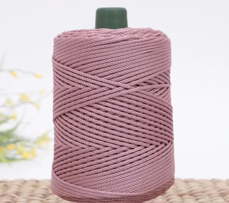 A spool of pink crochet ice rope with a green cap resting on a woven mat.