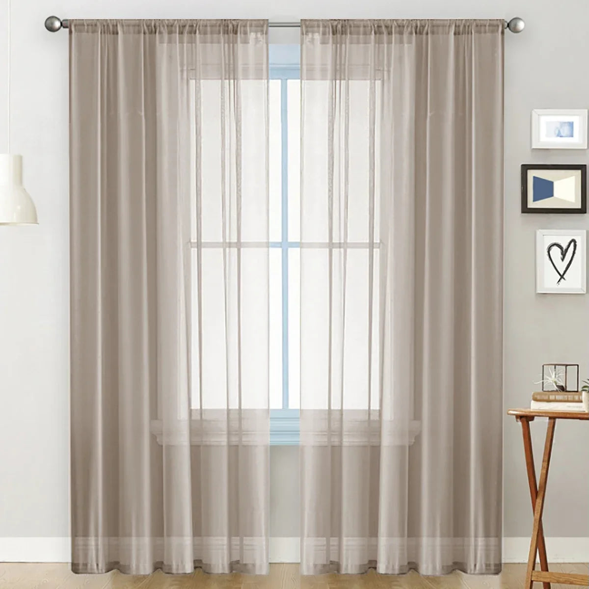 A pair of floor-length, sheer taupe curtains with rod pockets hanging over a window.