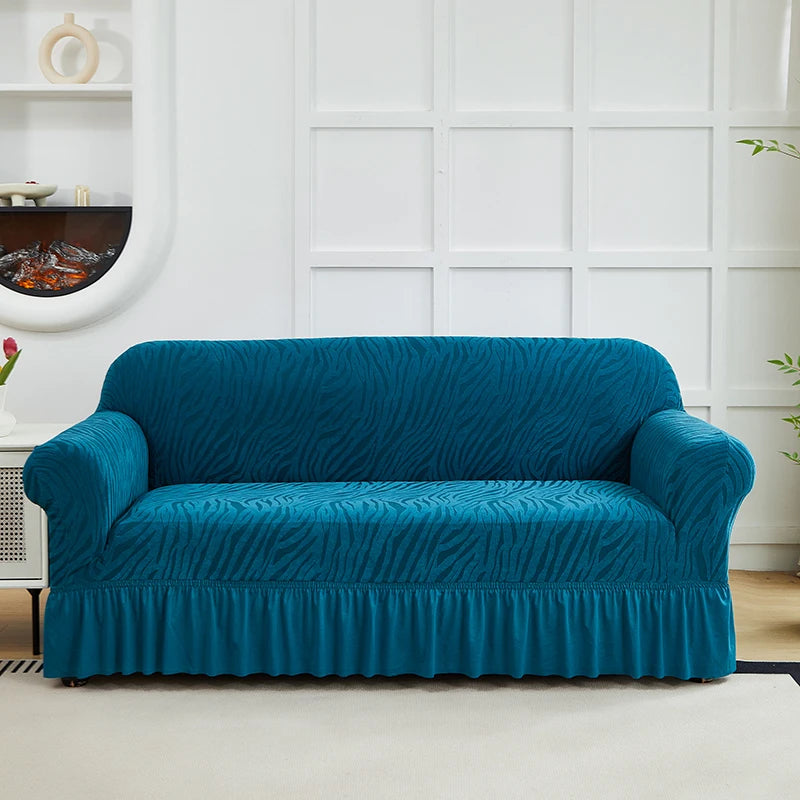 A teal anti-slip jacquard sofa slipcover displayed on a white couch in a bright room.