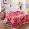 A pink rose and peony floral fleece blanket is draped over a bed, next to a bedside table.