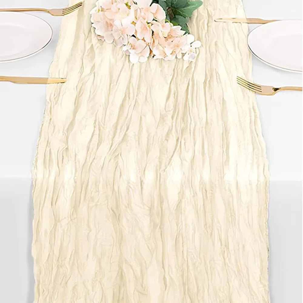A cream cheesecloth table runner with a textured, wrinkled finish, featuring pink flowers and gold cutlery.