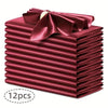 A stack of twelve deep red silky satin dinner napkins with a matching bow on top.
