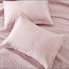 A set of soft, quilted pink cotton pillow covers resting on a textured fabric.