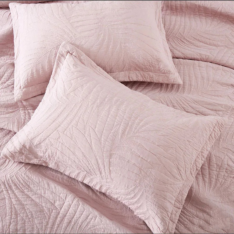 A set of soft, quilted pink cotton pillow covers resting on a textured fabric.