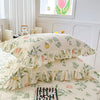 Two floral cotton pillow covers in cream and green leaves are displayed on a bed.