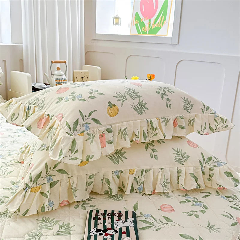 Two floral cotton pillow covers in cream and green leaves are displayed on a bed.