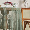 A round floral lace tablecloth in sage green with a tatting weave displayed on a wooden table.
