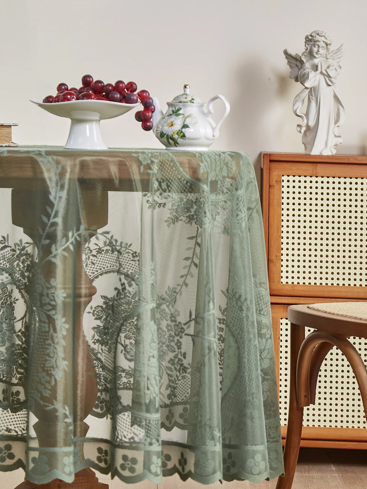 A round floral lace tablecloth in sage green with a tatting weave displayed on a wooden table.