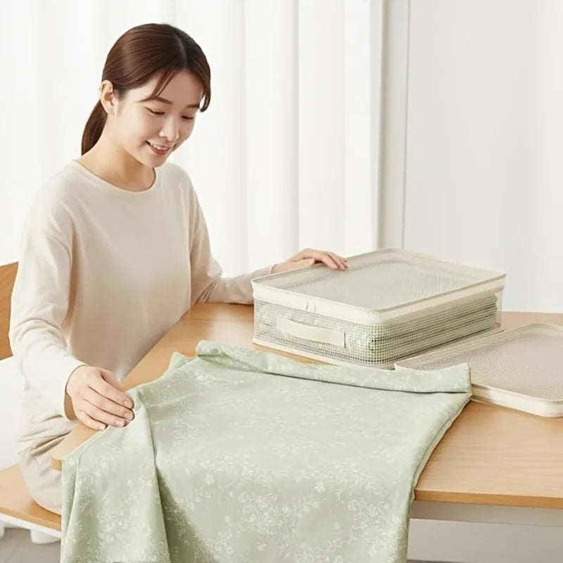A woman is folding a light green blanket into a foldable storage bag on a wooden table.