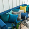 A collection of teal, blue, and yellow velvet throw pillows arranged on a deep blue sofa.