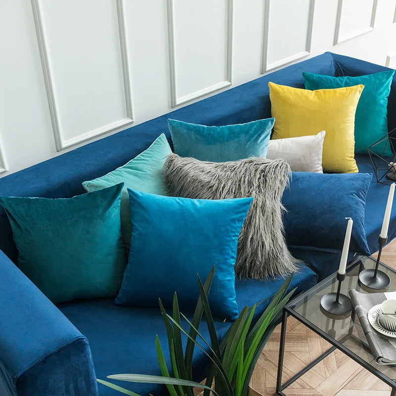 A collection of teal, blue, and yellow velvet throw pillows arranged on a deep blue sofa.