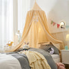 A princess hanging bed canopy in light yellow fabric draped over a bed with soft bedding and pillows.