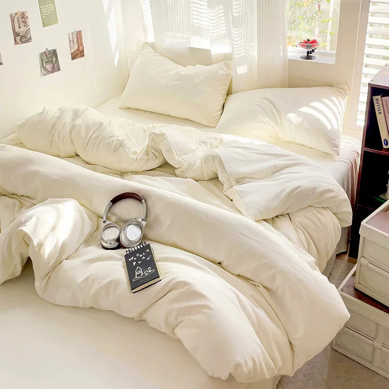 A white solid cotton bed linen set with fluffy pillows and bedding is displayed in a bright room.
