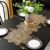 Gold leaf patterned placemats and cutlery set on a black table with a floral centerpiece.