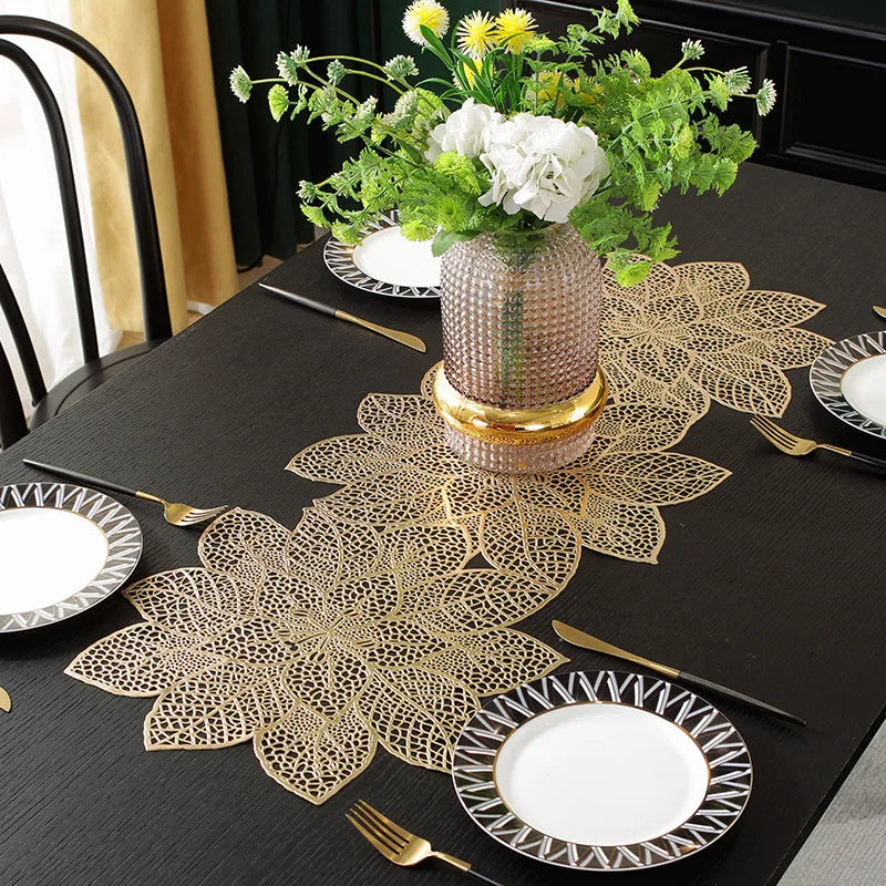 Gold leaf patterned placemats and cutlery set on a black table with a floral centerpiece.