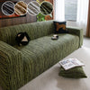 A dark olive green jacquard plush elastic sofa cover with a patterned fabric and a brown accent pillow.