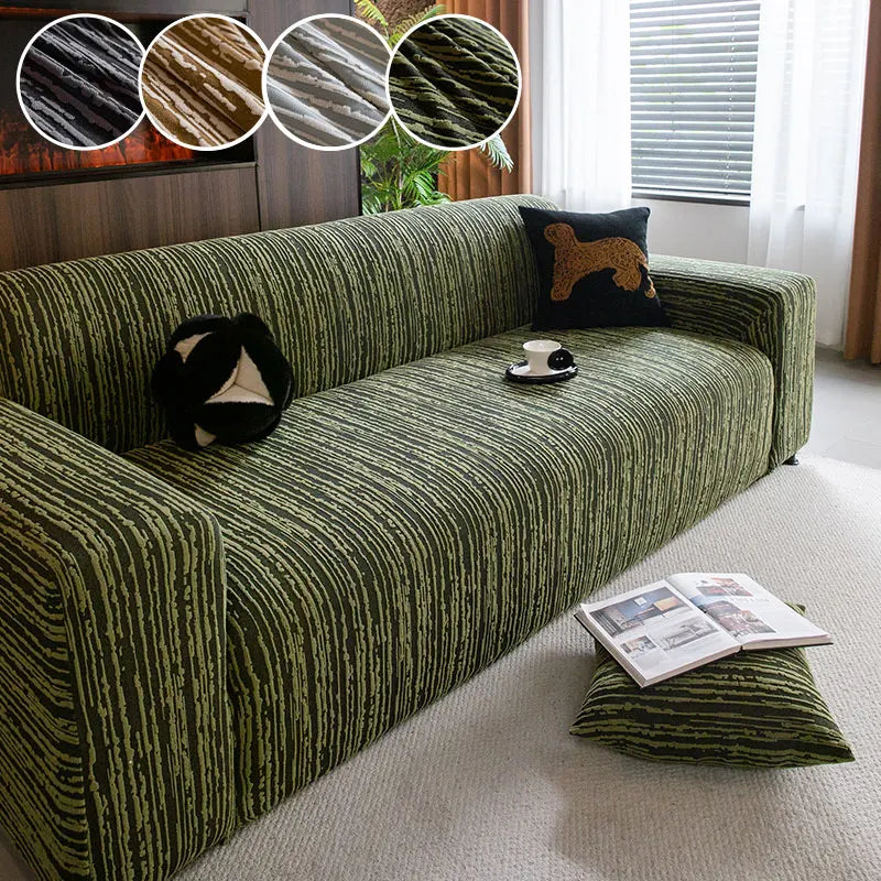A dark olive green jacquard plush elastic sofa cover with a patterned fabric and a brown accent pillow.