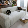 A light gray Jacquard plush elastic sofa cover with striped texture and a dark brown accent pillow on a modern sofa.