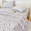 A white and gray floral quilted bedspread with light blue trim and matching pillows on a bed.