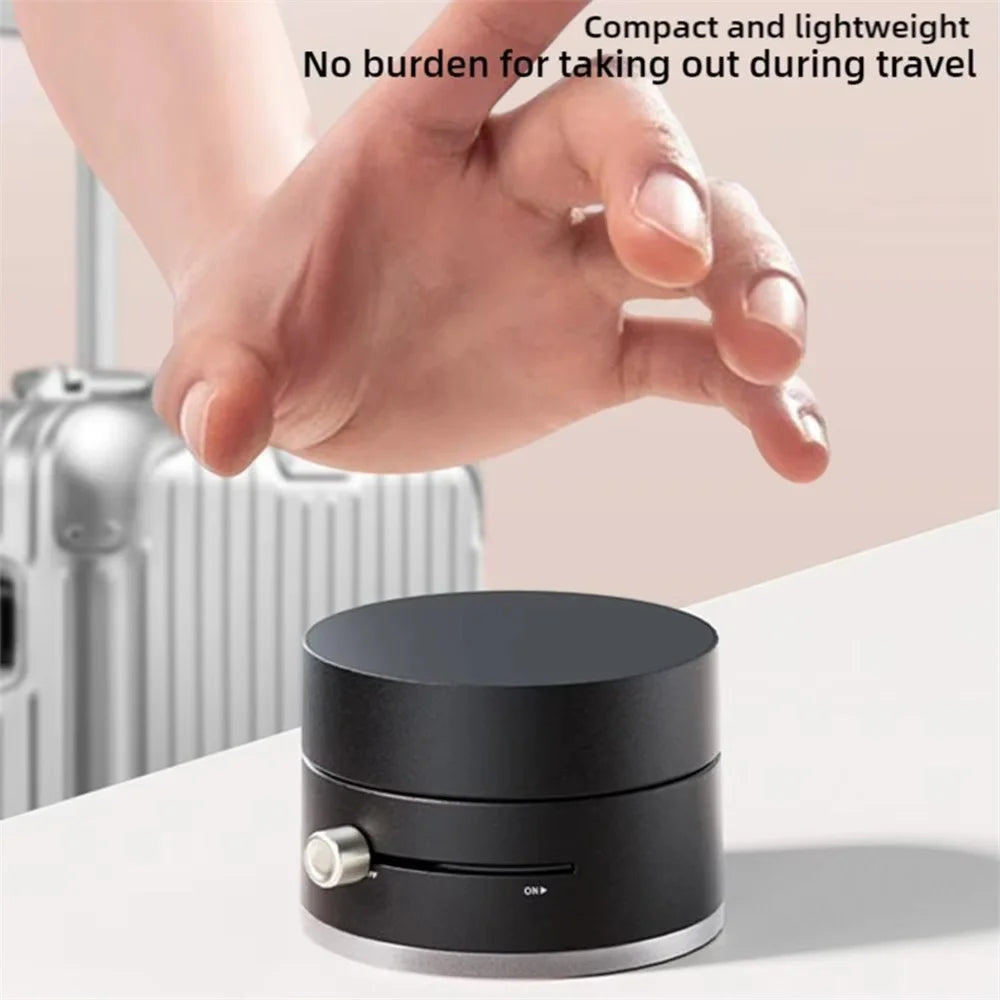 A compact, black foldable magnetic phone stand with a vacuum suction base is shown next to a hand.