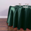 A dark emerald green satin round table cloth set for elegant decor with white plates and silverware.