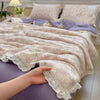 A hand is holding a light purple summer floral print quilt blanket with white lace trim.