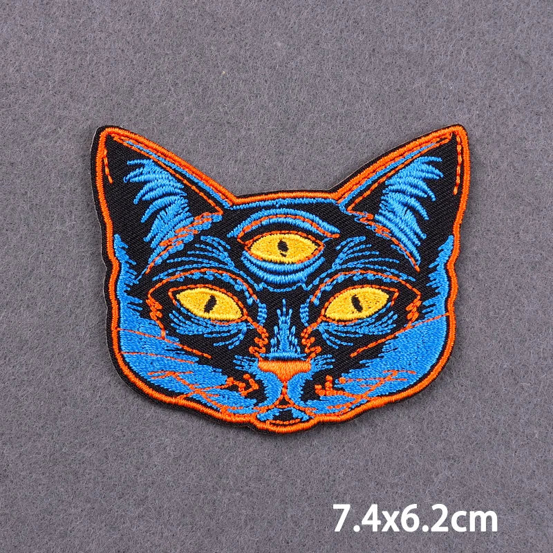 A black and blue cat face embroidery patch with yellow eyes on a gray fabric background.