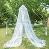 A large white dome mosquito net is set up outdoors in a grassy park area.