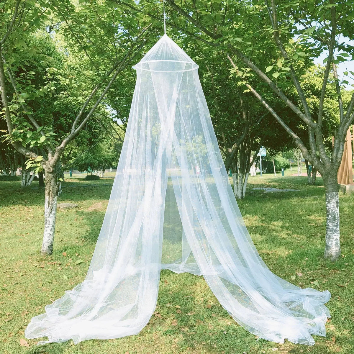 A large white dome mosquito net is set up outdoors in a grassy park area.