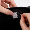 Hands are using a needle to attach magnetic snap fasteners onto a black bag or purse.