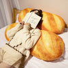 A person is resting their head on a large, golden-brown plush baguette pillow with a sign that reads Rayon de Soleil.