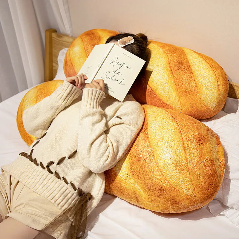 A person is resting their head on a large, golden-brown plush baguette pillow with a sign that reads Rayon de Soleil.