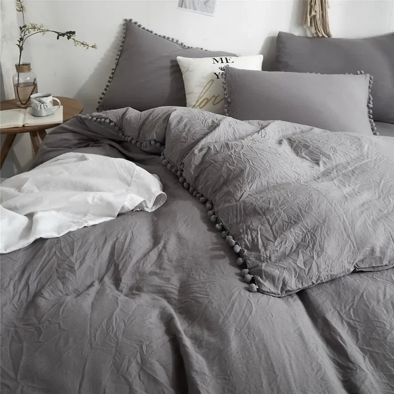 A gray duvet cover set featuring pom-pom trim and decorative pillows on a bed.