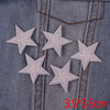 Five glitter iron-on embroidered star patches are shown on denim fabric with visible stitching.