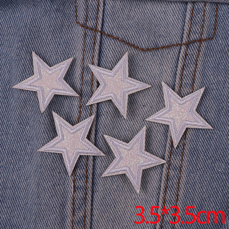 Five glitter iron-on embroidered star patches are shown on denim fabric with visible stitching.