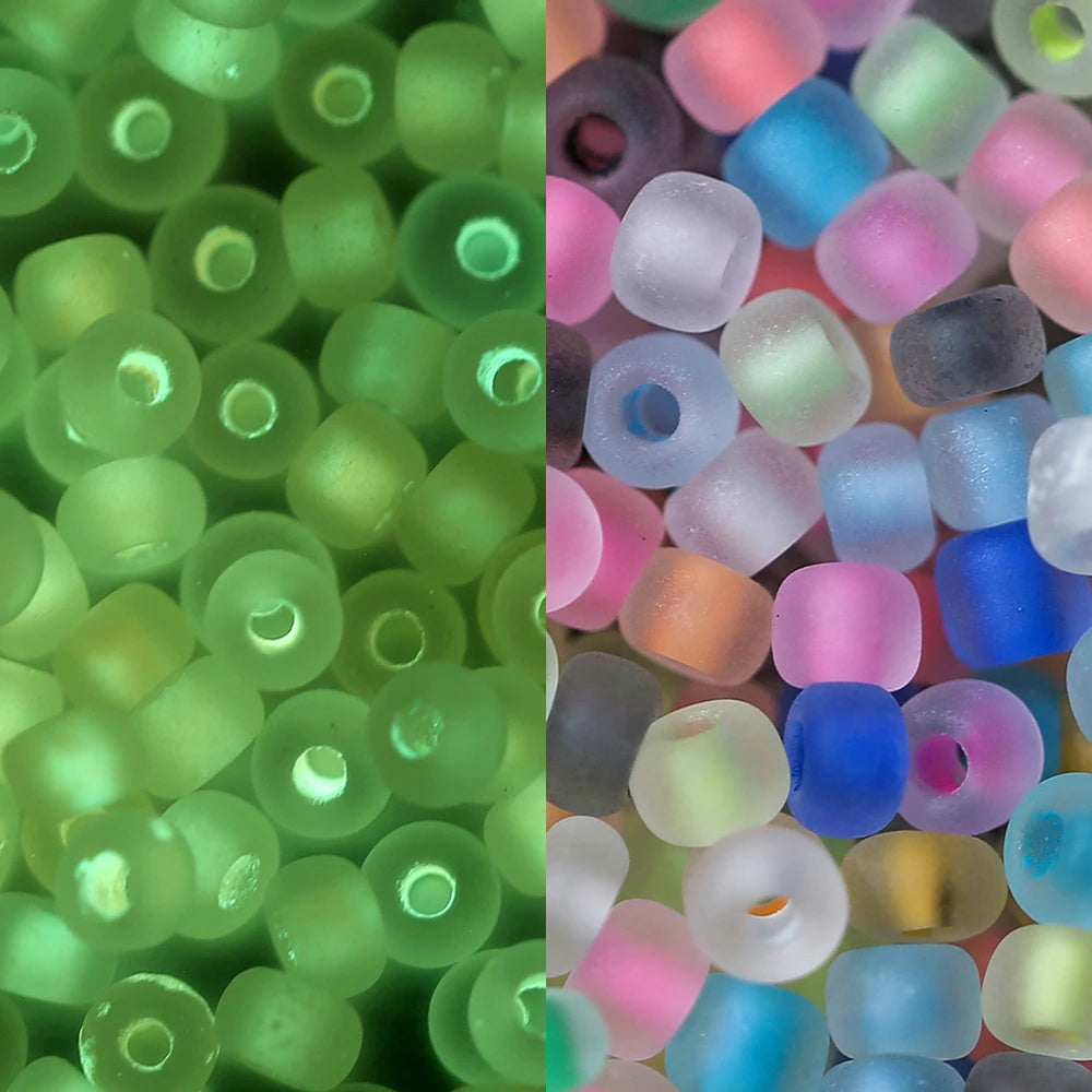 A close-up view of a 600-pack of 3mm glow-in-the-dark glass seed beads in various shades of green, pink, blue, and purple.