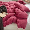 A pink quilted duvet cover set with pom-pom decoration displayed on a white bed.