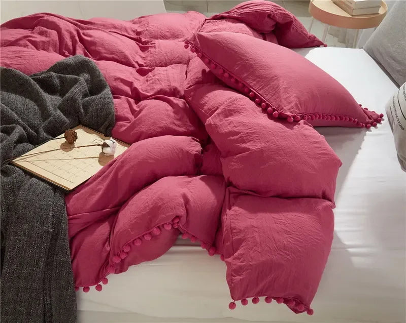 A pink quilted duvet cover set with pom-pom decoration displayed on a white bed.
