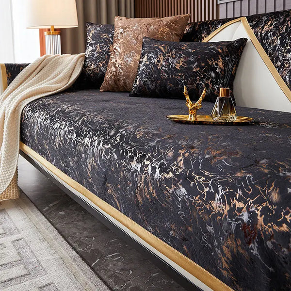 A dark velvet sofa cover featuring a marbled pattern in black, gold, and white tones.