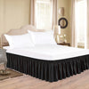 A white bed with a black ruffle skirt and adjustable elastic belt in a bedroom setting.