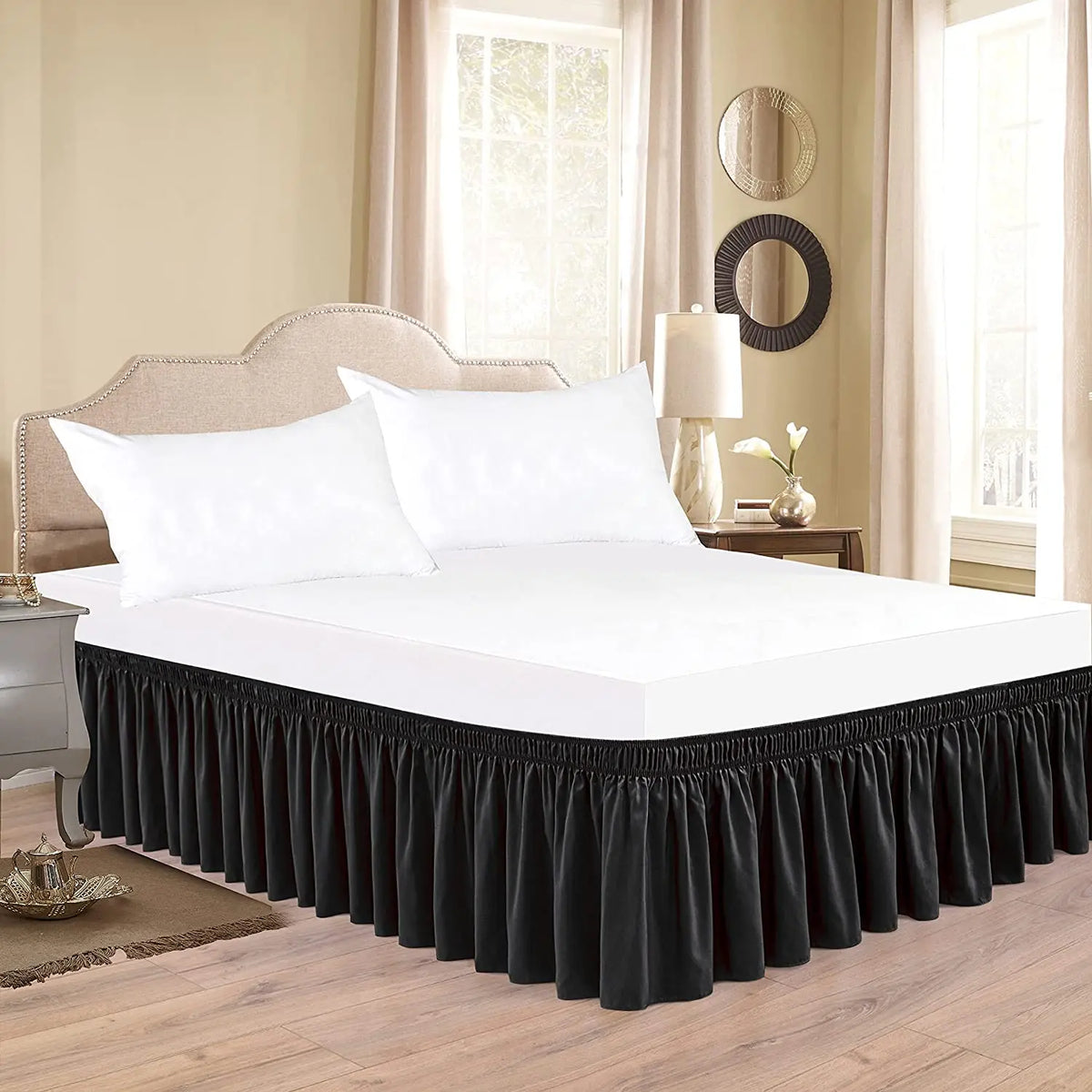 A white bed with a black ruffle skirt and adjustable elastic belt in a bedroom setting.