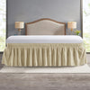 A beige wrap around elastic bed skirt covering a bed with a wooden headboard and bedside lamps.