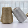 Two spools of metallic silk crafting yarn, one gold and one gray, lying on a white surface.