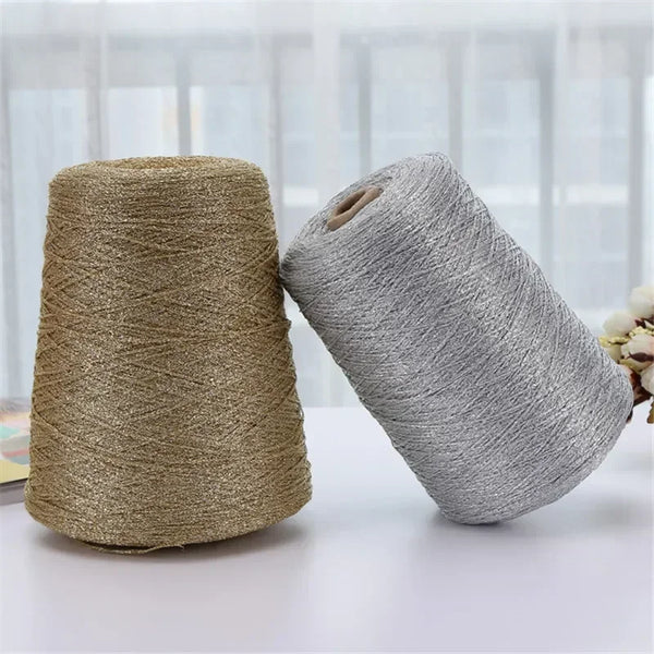 Two spools of metallic silk crafting yarn, one gold and one gray, lying on a white surface.