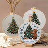 A hand embroidery kit featuring a stitched Christmas tree and a bear, displayed on a wooden easel.