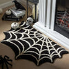 A black and white spider web patterned Halloween door mat placed on a light wood floor.
