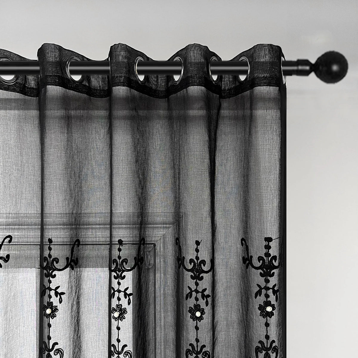 Black sheer curtain featuring delicate pearl and lace embroidery hanging from a rod.
