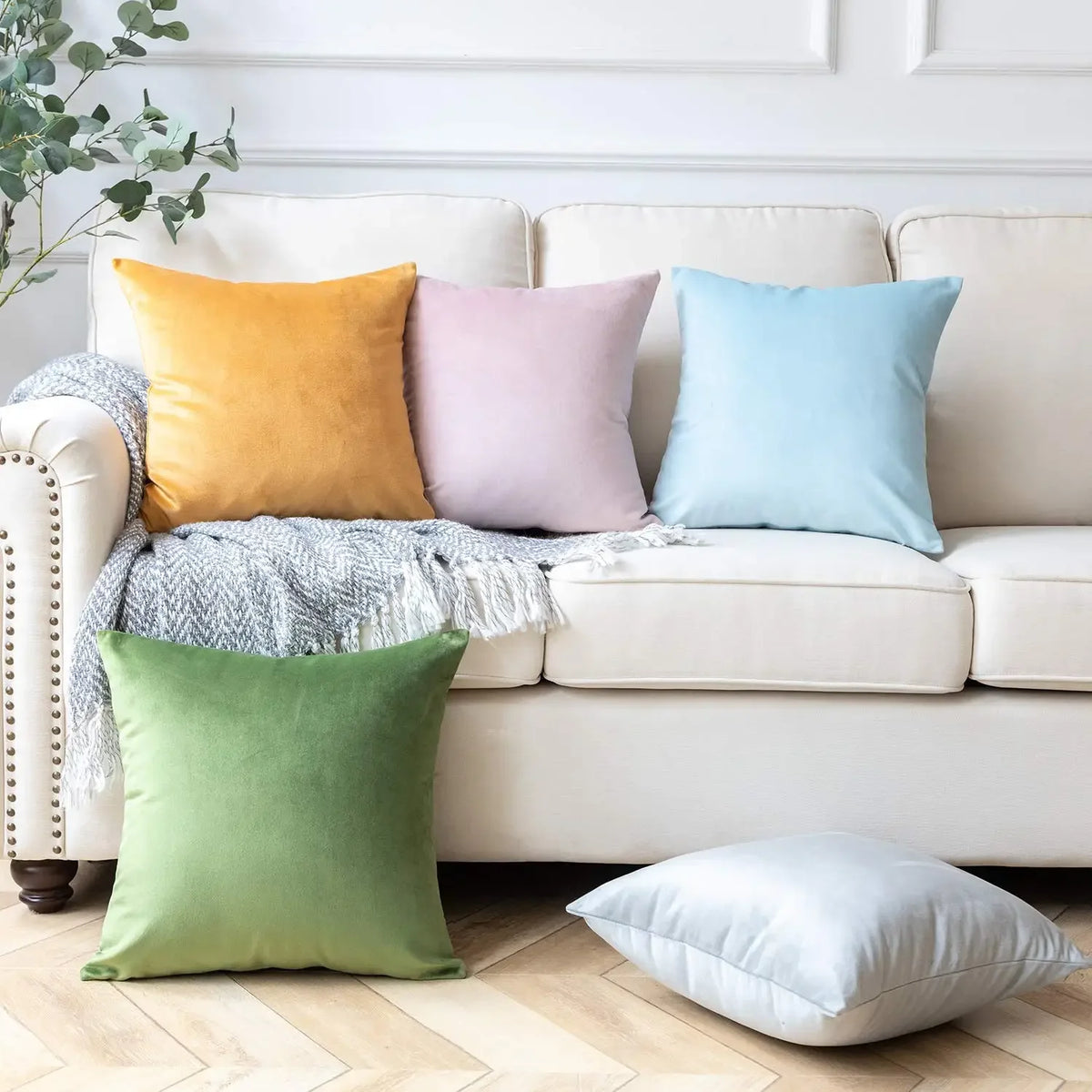 A collection of velvet throw pillows in yellow, pink, blue, and green resting on a light-colored sofa.
