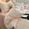 A pink plaid duvet cover set with matching pillowcases and a stuffed animal on a bed.