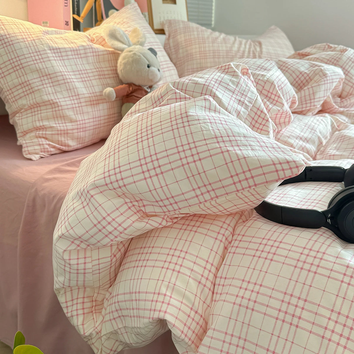 A pink plaid duvet cover set with matching pillowcases and a stuffed animal on a bed.